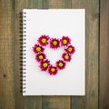 Heart sumbol of flowers on notebook isolated on wood background. Flat lay, Top view.