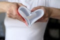 Heart is a symbol of love made of bent sheets of a notebook, female hands are holding near the chest. Valentine`s Day.