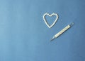 Heart symbol made from white pills and a medical mercury thermometer on a blue background with copy space. Concept for the treatme Royalty Free Stock Photo