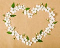 Heart symbol made of white spring flowers and green leaves on brown paper background. Flat lay Royalty Free Stock Photo