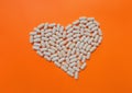 Heart of white pills on vivid orange background. The concept of dietary supplements