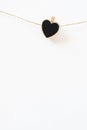 Heart wooden black chalkboard clothespin on rope twine on white wall, vertical. Close-up detail garland decoration. Cute postcard