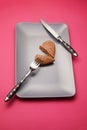 Heartbreaker concept image: heart shaped cookie on plate with fork and knife over pink background