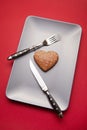 Heartbreaker concept image: heart shaped cookie on plate with fork and knife over red background