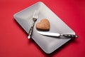 Heartbreaker concept image: heart-shaped cookie on plate with fork and knife over red background