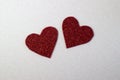 Hearts cut out of red glitter paper on a sparkly white background close up