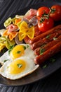 hearty breakfast: fried eggs, sausages, farfalle pasta and tomatoes close-up. vertical Royalty Free Stock Photo