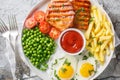 Hearty dinner of grilled loin steak with green peas, fried eggs, french fries, fresh tomatoes and sauce close-up in a plate. Royalty Free Stock Photo