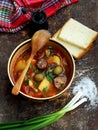 Hearty homemade soup with potatoes, carrots, sausages and olives in a clay bowl on a wooden background. Royalty Free Stock Photo