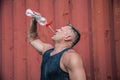 Heat exhaustion bodybuilder, is raising a bottle of water. He is pouring out aqua to his mouth to cool himself off