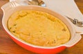 Heat resistant, red bowl filled with baked, corn pudding with cilantro and chorizo filling