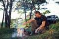 Heating by the fire. Man in black shirt near the campfire in the forest at his weekend time