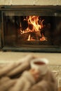 Heating house with wood burning stove. Burning fireplace close up and blurred hands with cup of warm tea , autumn hygge. Relaxing Royalty Free Stock Photo