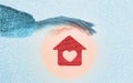 Heating of houses. A woman's hand protects a red little house with a heart in a warm round glow. Blue background