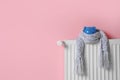 Heating radiator with piggy bank and knitted scarf near color wall
