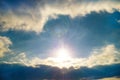 Shining rays of the sun against a white cloud and blue sky Royalty Free Stock Photo