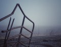 Rusty bent metal fence near railroad tracks in the fog. Royalty Free Stock Photo