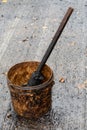 Heavily soiled road worker bucket with brush and oily liquid while paving new asphaltand oily liquid w