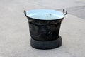 Heavily used old partially rusted black cauldron with two metal handles left on top of old car tyre