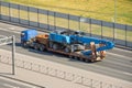 Heavy blue excavator long boom bucket on transportation truck with rubber wheels long trailer platform on the highway in the city