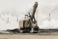 Heavy bucket mining excavator on a crawler track against a background of dense factory strong smog with smoking chimneys