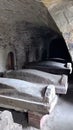 Heavy coffins lie on sand floor in an very small old dusty cemetery crypt in a cave