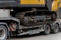 Heavy construction machine with steel tracks loaded onto long platform trailer Royalty Free Stock Photo