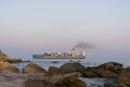 A heavy container ship with cargo enters the port by tug. Port of Yuzhny. Coastal stones in the foreground. Selective focus. 2019.