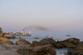 A heavy container ship with cargo enters the port by tug. Port of Yuzhny. Coastal stones in the foreground. Selective focus. 2019.