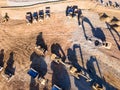 Heavy dump trucks, bulldozers, and excavators on yellow clay construction site. Long shadows on the ground. Top view at sunset