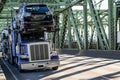 Heavy duty big rig blue car hauler semi truck transporting cars on two level modular semi trailer driving on the truss bridge at Royalty Free Stock Photo