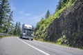 Heavy duty big rig semi truck with dry van semi trailer running on the turning winding mountain highway road with rocks and trees