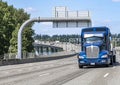 Heavy-duty blue big rig semi truck transporting industrial cargo on step down semi trailer driving on the long bridge across the Royalty Free Stock Photo