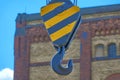 Heavy duty iron hook in a black and yellow fixation in front of an intentionally blurred facade of an industrial building