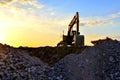 Heavy excavator bucket working in quarry on a background of sunset and blue sky. Mobile jaw stone crusher by the construction site