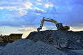 Heavy excavator working in quarry on a background of sunset and blue sky.