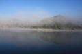 Heavy fog-covered rolling hills wit a reflection on a calm reflective lake water