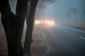 Heavy fog on the road in the early morning. City street with cars in the distance is in poor visibility. The bright light of the Royalty Free Stock Photo