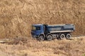 A heavy four-axle dump truck of blue drives along a dirt road against the background of a clay embankment. Career and road works.