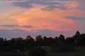 Closeup of a cloudy orange and purple sky over a landscape of bushy trees