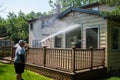 Heavy husband power washing large windows on the back of a house over a brown wooden deck with a pressure washer.