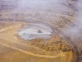 Heavy machinery working at the bottom of an open pit mine on a day with a lot of fog and rain