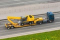 Heavy new yellow excavator long boom bucket on transportation truck with rubber wheels long trailer platform on the highway in the Royalty Free Stock Photo