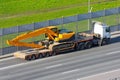 Heavy new yellow excavator long boom bucket on transportation truck with long trailer platform on the highway in the city Royalty Free Stock Photo