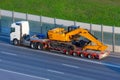 Heavy new yellow excavator on transportation truck with long trailer platform on the highway in the city Royalty Free Stock Photo