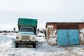 A heavy old blue dump truck is parked next to a building amid white snow, waiting for loading to begin Royalty Free Stock Photo