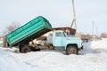 Heavy old blue dump truck with raised body close-up on the background of a snowy road, side view