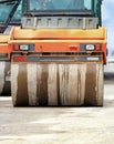 A large and heavy orange vibratory roller is moving along the road