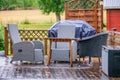 Heavy rain at wooden terrace with summer chairs, wooden table. Blurry green forest at background. Everything is very wet. Royalty Free Stock Photo