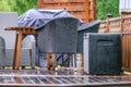 Heavy rain at wooden terrace with summer chairs, wooden table, grill covered against of rain. Blurry green forest at background. Royalty Free Stock Photo